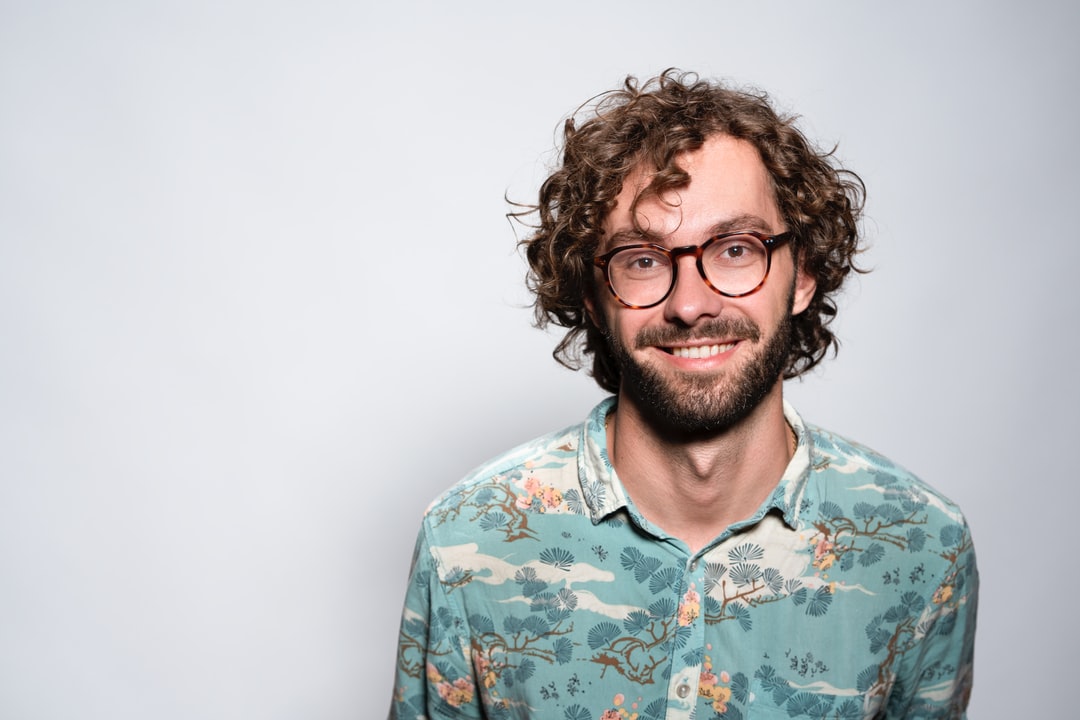 young man wearing glasses smiling at camera wearing a Hawiian dress shirt