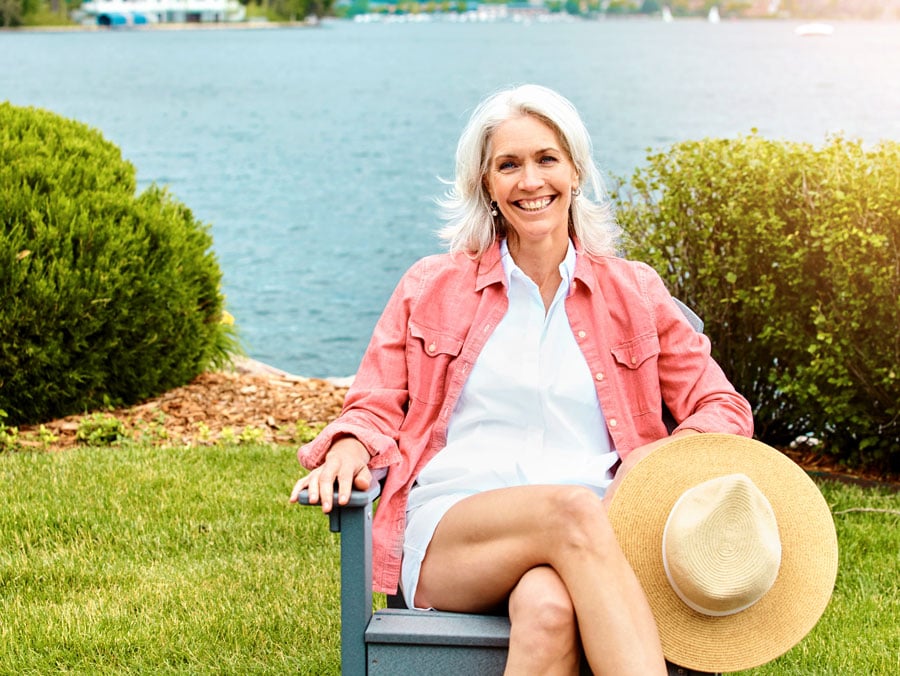 Smiling woman relaxing by a lake, representing a smooth cataract surgery recovery and return to daily activities