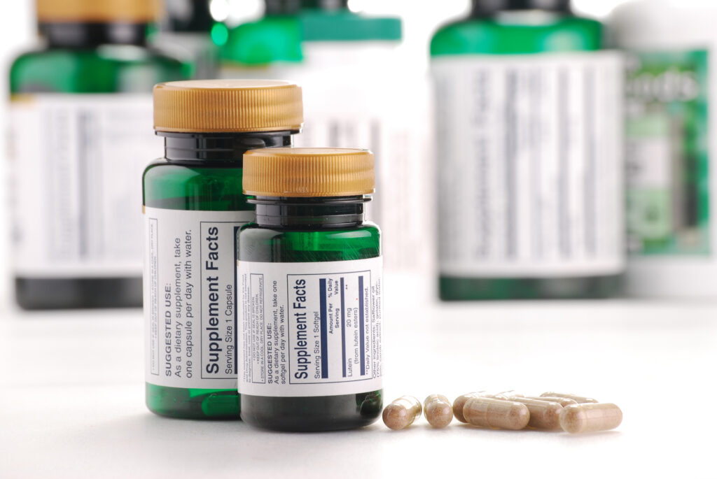 Green supplement bottles labeled “Supplement Facts” alongside a few softgel capsules, representing eye vitamins