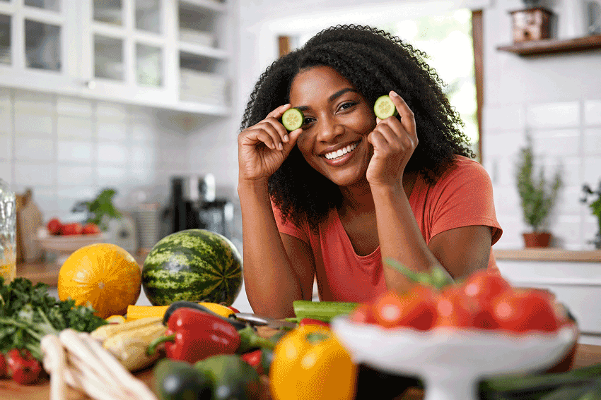Woman holding cucumber slices in a kitchen surrounded by some of the best foods for glaucoma