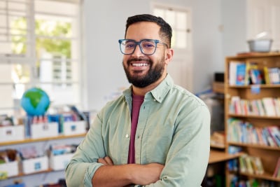 Man with eyeglasses has crossed arms at a library and is thinking about getting a comprehensive eye exam.