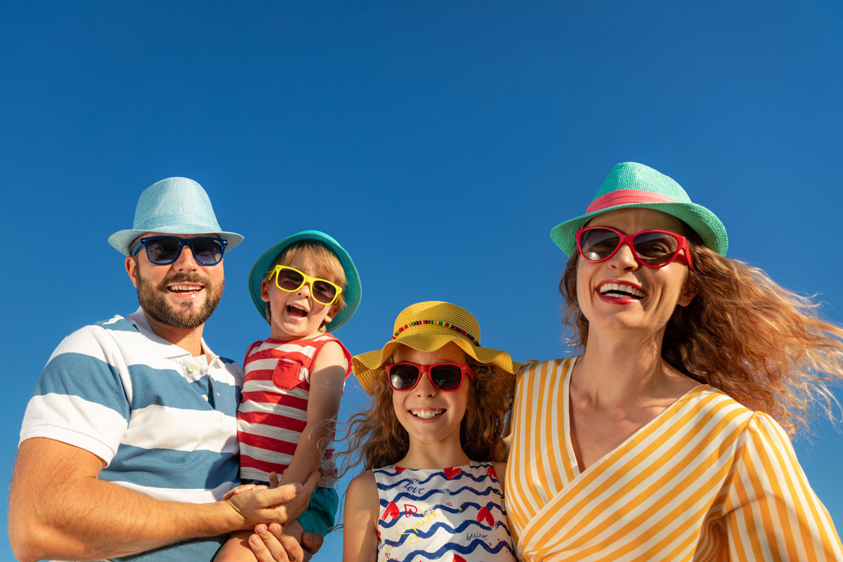 Smiling family wearing hats and sunglasses outdoors on a sunny day, symbolizing children’s eye protection and summer eye safety.