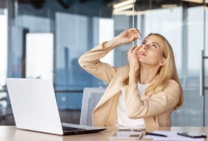 Woman applying lubricating eye drops at her desk—how to cure dry eyes permanently with the right drop plan