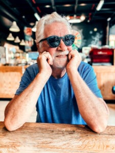 Smiling senior man wearing UV400 sunglasses at a café—sunglasses after cataract surgery