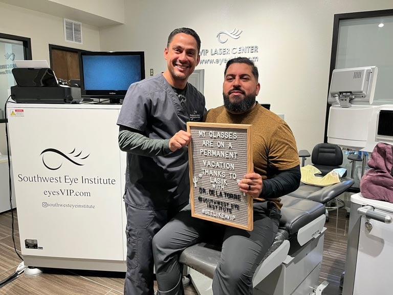 ASIK patient seated in exam chair at Southwest Eye Institute holding a sign that says “My glasses are on a permanent vacation,” celebrating successful LASIK eye surgery in El Paso.