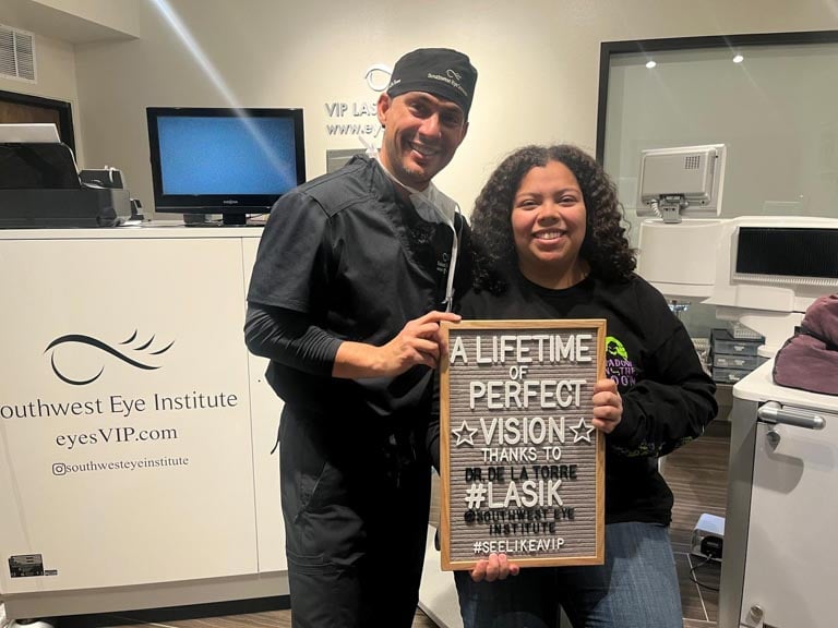 Smiling LASIK patient holding a “A lifetime of perfect vision” sign with Southwest Eye Institute surgeon after laser eye surgery in El Paso, Texas.