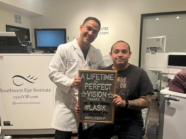 LASIK patient and Southwest Eye Institute surgeon holding a sign that reads “A lifetime of perfect vision,” following laser eye surgery in El Paso.
