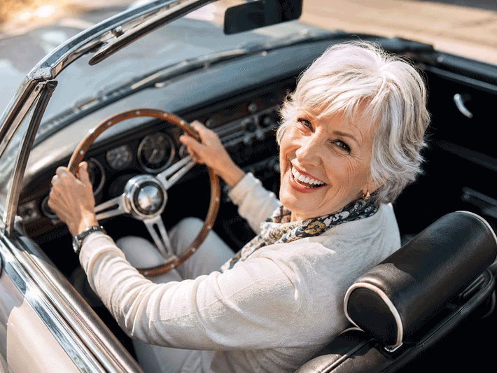 Senior woman smiling while driving a classic convertible in bright sunlight, illustrating outdoor light sensitivity and photophobia causes for Southwest Eye Institute.